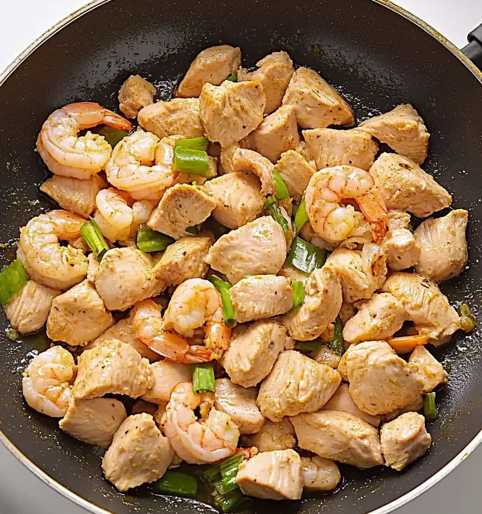 How to make a delicious chicken and shrimp Alfredo at home 11 A skillet filled with cubed chicken, shrimp, and chopped green onions being sautéed for Alfredo pasta.