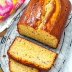A freshly baked banana bread loaf with a golden-brown crust, sliced to reveal a soft, moist texture with specks of mashed banana.